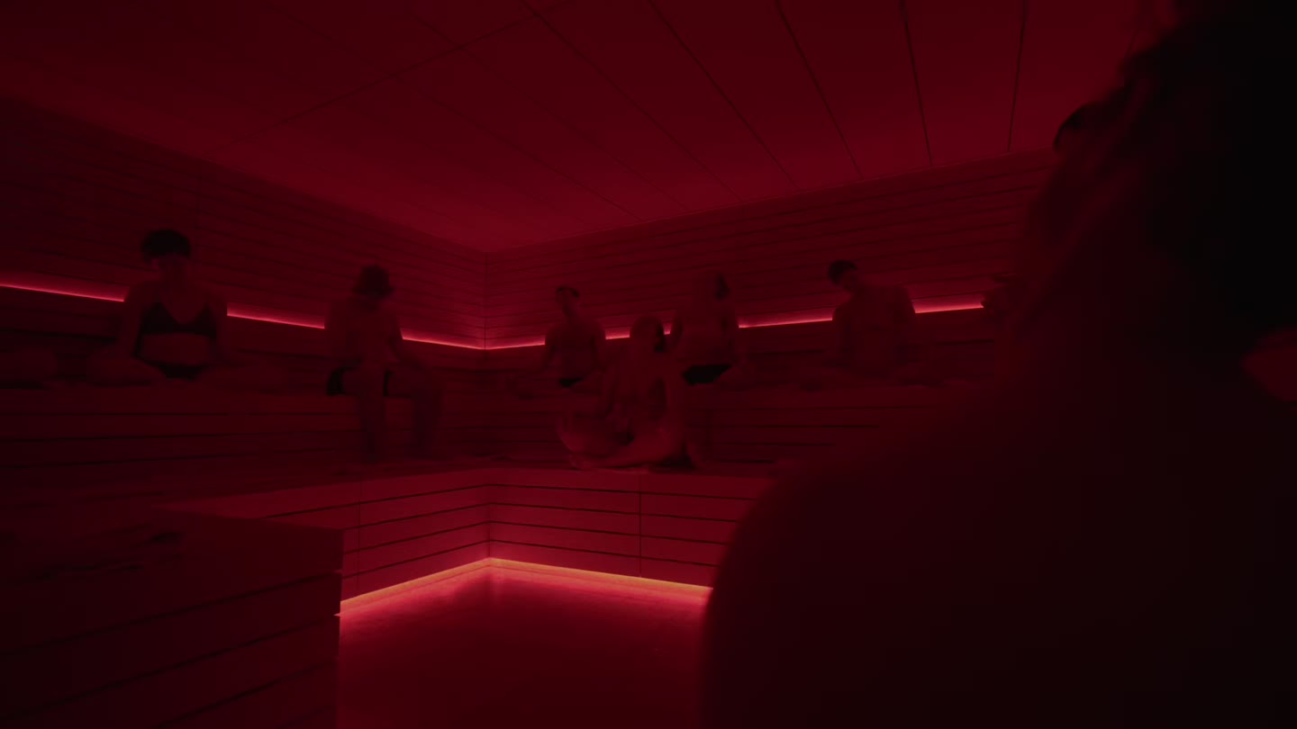 Un grup assegut junt als bancs de la sauna il·luminada en vermell d'ILO STUDIOS