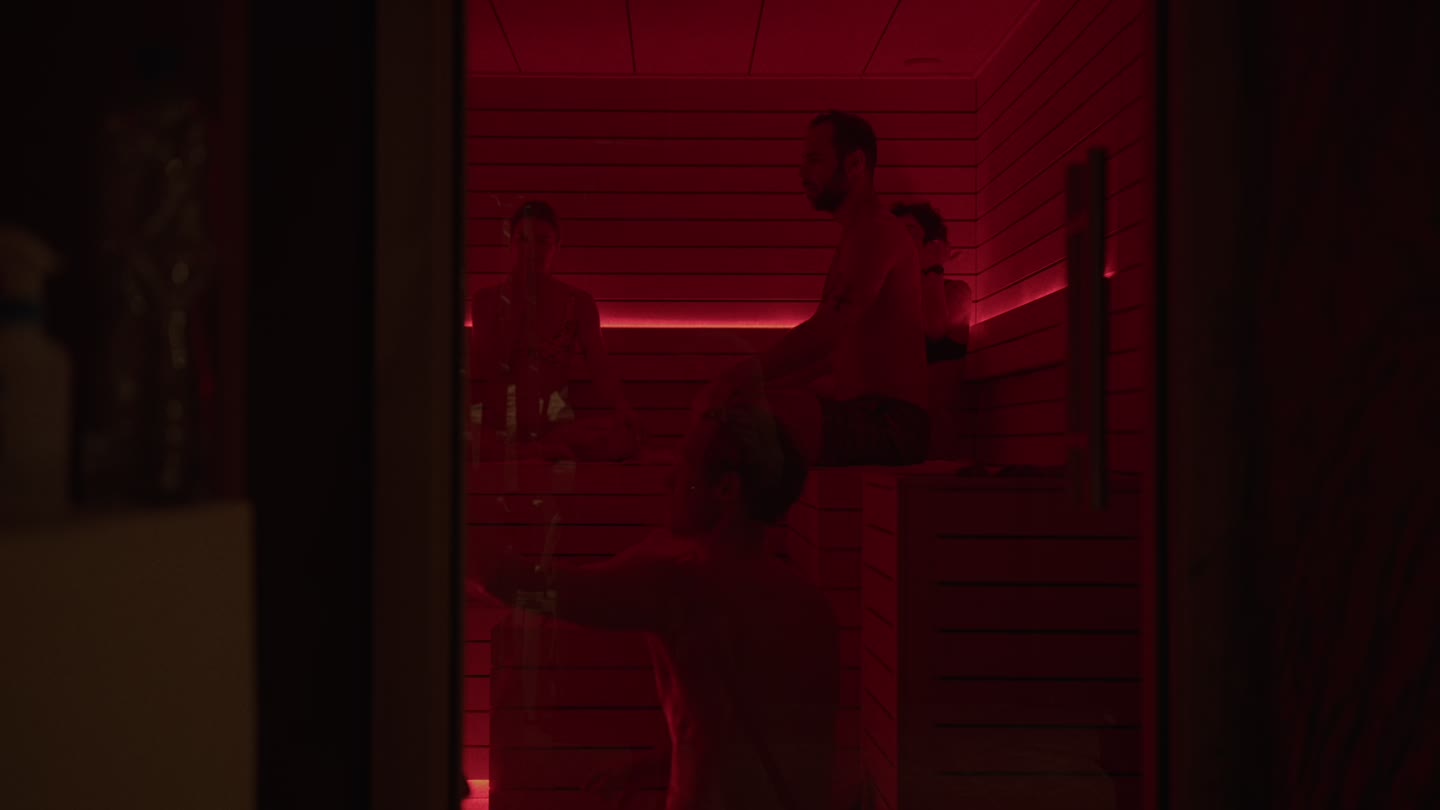 Persones a la sauna il·luminada en vermell d'ILO STUDIOS, vistes a través de la porta oberta