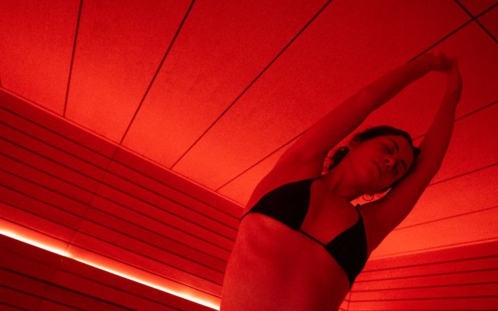 A guest stretching in the red-lit sauna at ILO STUDIOS
